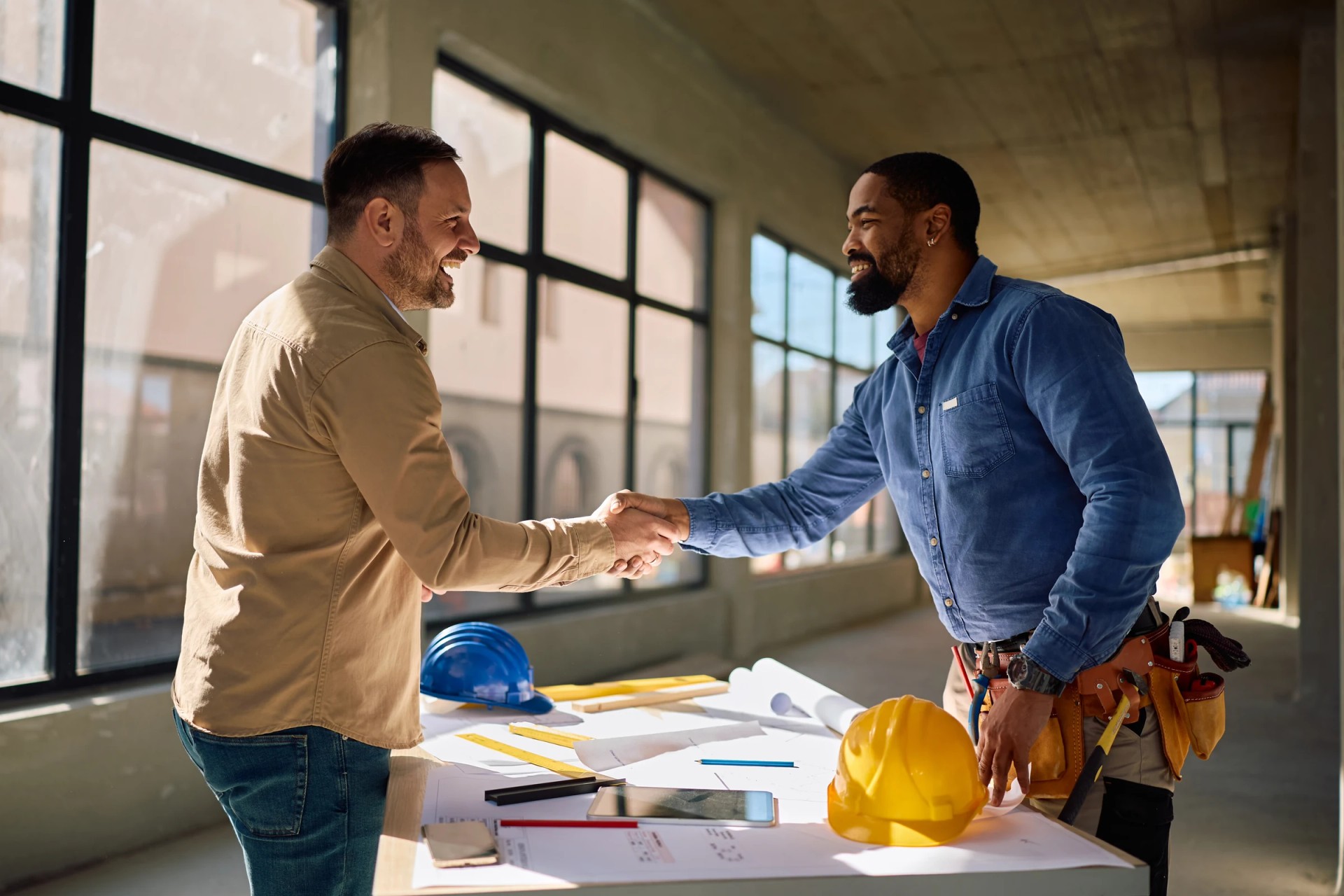 Cliente e construtor apertando as mãos sobre a planta da obra
