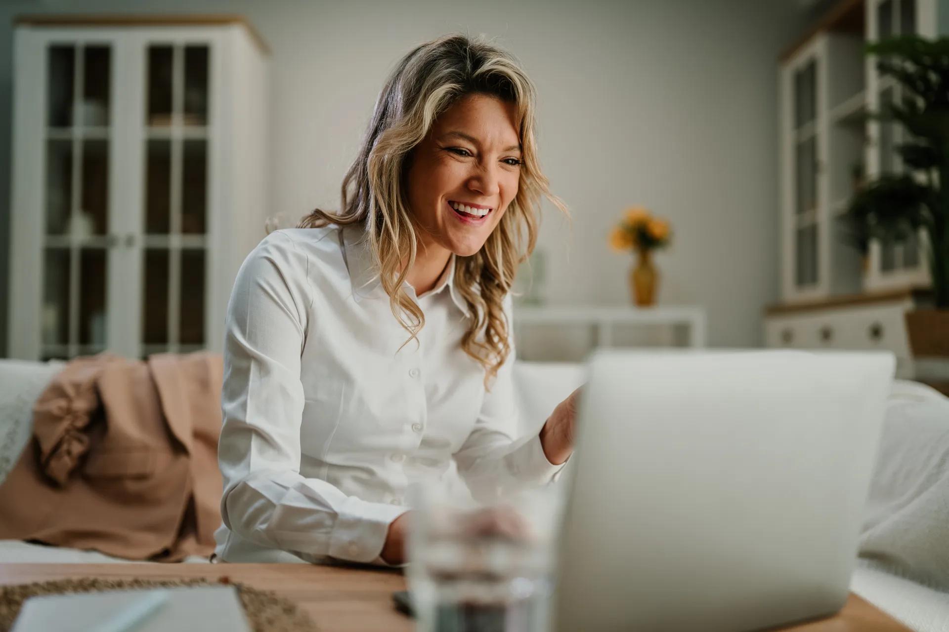 Mulher sorrindo ao acompanhar a proposta pelo notebook em casa