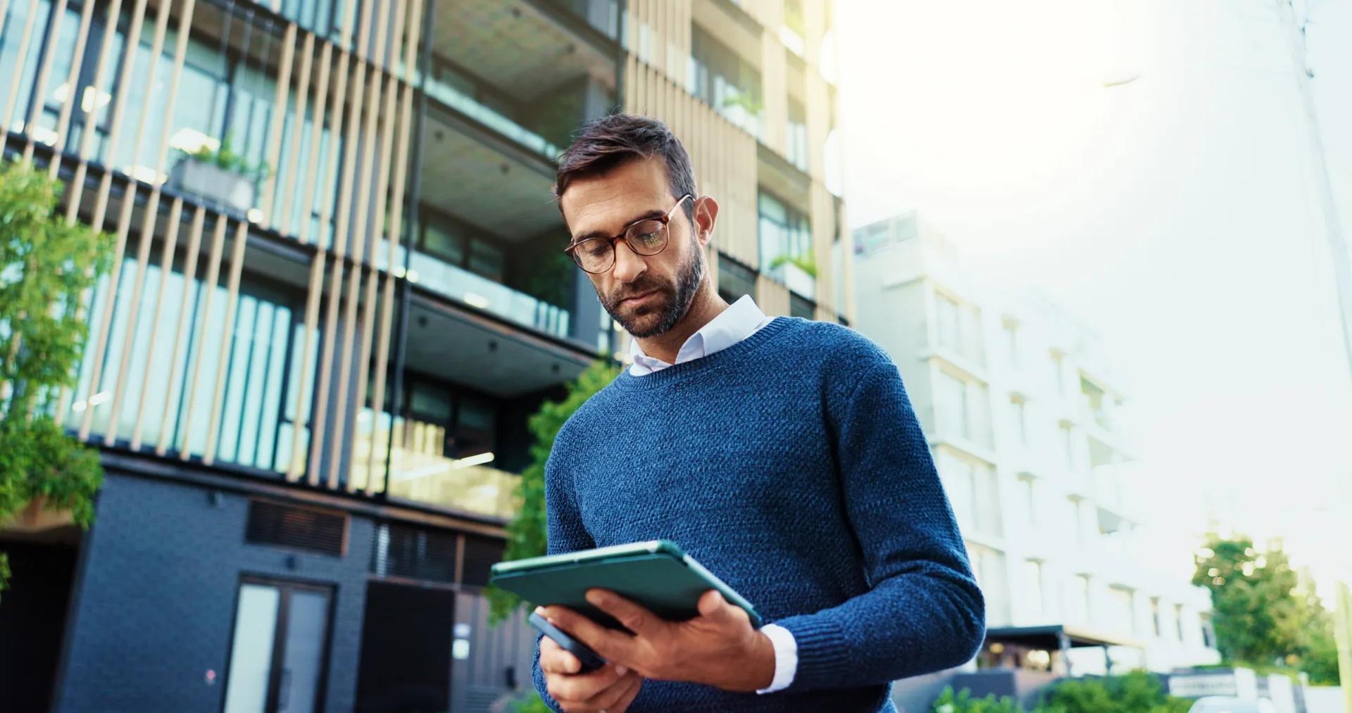 Homem consultando um tablet em frente à fachada de um edifício residencial