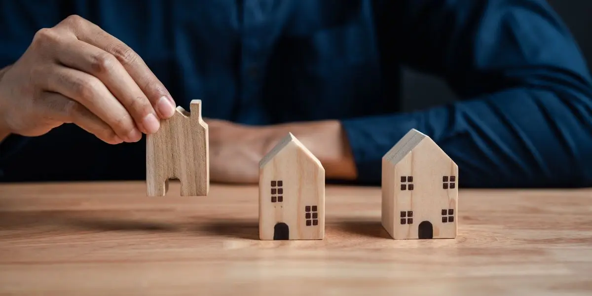 Uma pessoa colocando miniaturas de casas em madeira sobre uma mesa