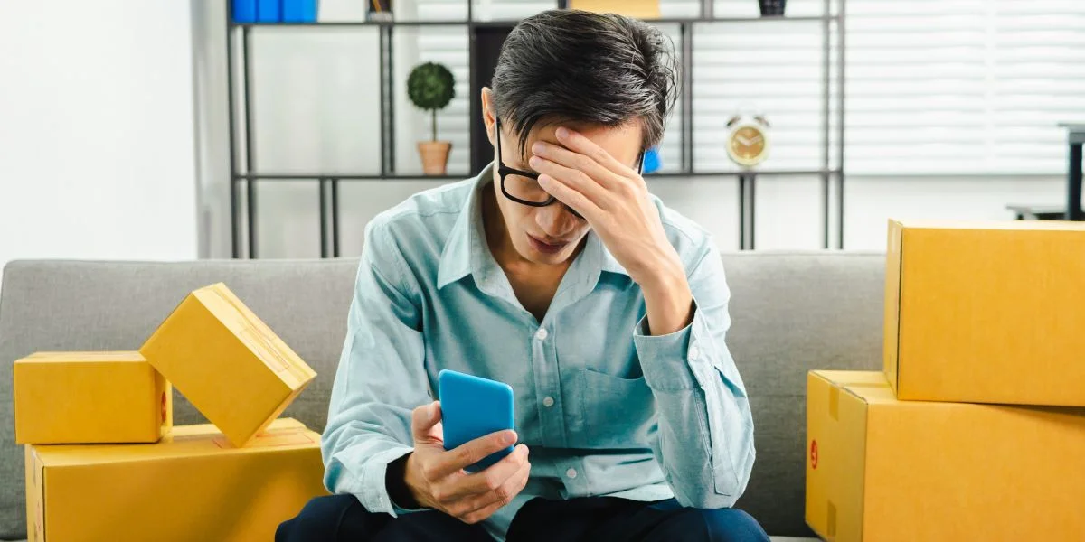 Um homem olhando para um celular e levando a mão até sua cabeça