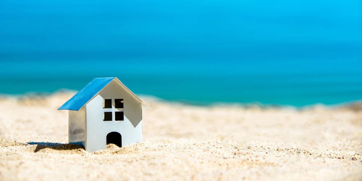 A miniatura de uma casa sobre a areia com o mar a seu fundo