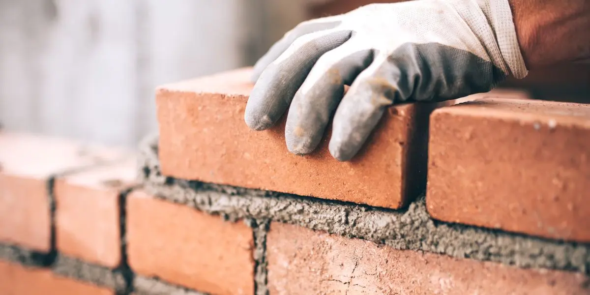 Uma pessoa assentando um tijolo em uma parede em construção